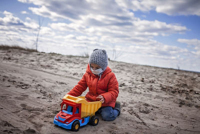 Boy with toy on sand at beach against sky