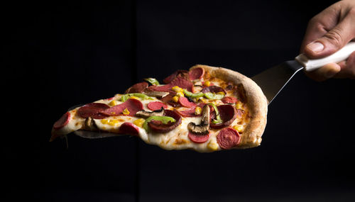 Close-up of hand holding pizza over black background