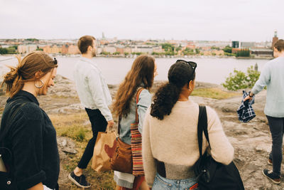 Smiling male and female friends walking on field by lake against sky