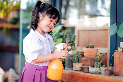 Smiling cute girl spraying water on potted plant