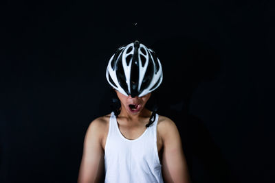Close-up of man yawning while wearing bicycle helmet against black background