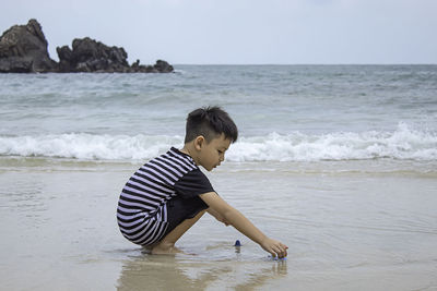 Rear view of boy at beach against sky