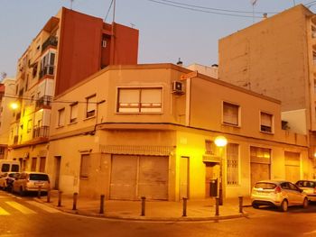 Illuminated street by buildings in city at dusk