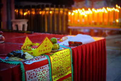 Offerings on table against lit candles in buddhist temple