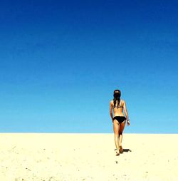 Woman standing on beach against blue sky