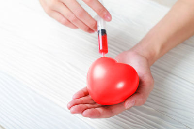 Cropped hands injecting heart shape over table