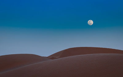 Full moon over sand dunes in sahara desert