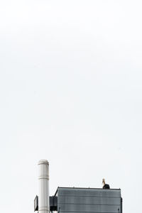 Low angle view of stork perching on metallic silo against clear sky