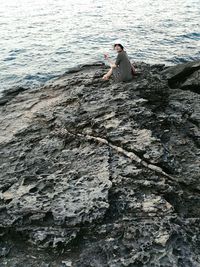 Man sitting on rock by sea against sky