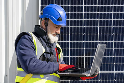 Engineer with helmet working on laptop at solar power station