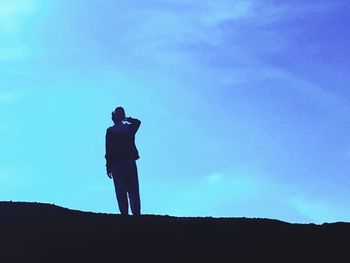 Silhouette of woman standing against blue sky