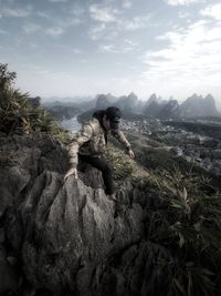 Rear view of woman sitting on rock against sky