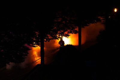 Silhouette person by trees against sky at night