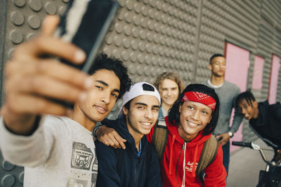 Happy male friends taking selfie with smart phone in city