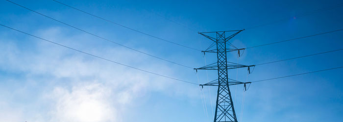 Low angle view of electricity pylon against blue sky