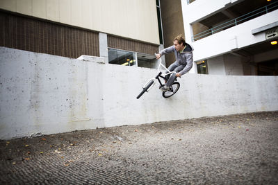 Cyclist performing stunt on retaining wall against building