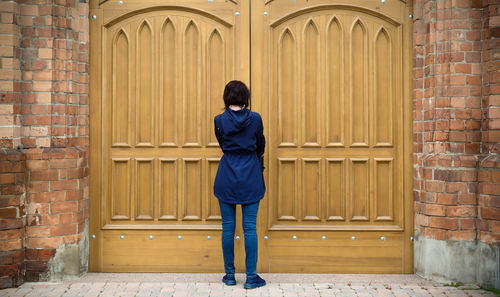 A woman is facing the huge gate of a catholic church trying to open the door.