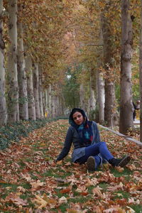 Full length of woman sitting on grassy field amidst trees during autumn