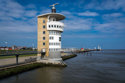 Lighthouse amidst sea and buildings against sky