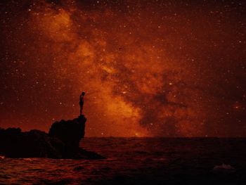 Silhouette rocks on sea against sky at night