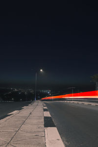 Illuminated road by street against sky at night