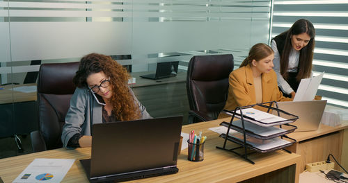 Curly business woman with glasses talking on phone in office. 