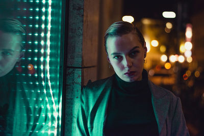 Portrait of young woman standing against illuminated wall