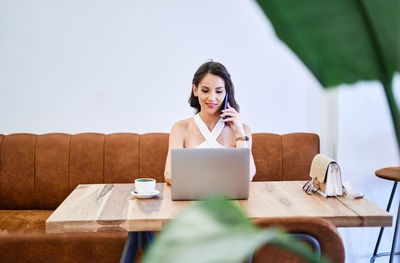 Female entrepreneur discussing business project on mobile phone while using netbook and working remotely at table in cafe