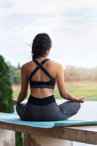 Rear view of young woman meditating on exercise mat at park