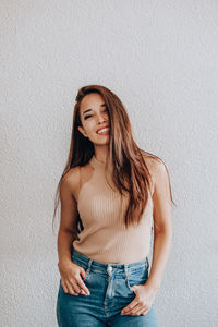 Portrait of a smiling young woman standing against wall