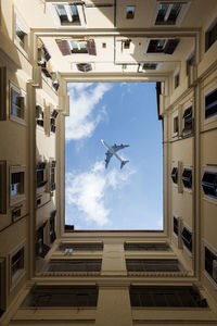 Directly below shot of building against airplane flying in sky