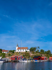 Houses by river and buildings against blue sky