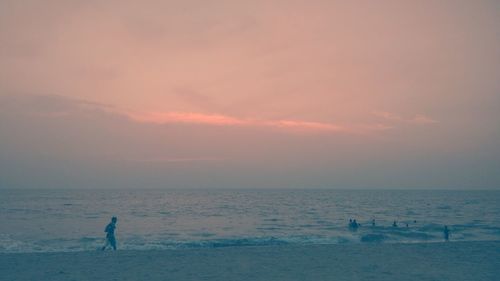 Man walking at beach against sky during sunset