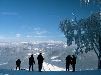 Silhouette people standing on snowcapped mountain against sky