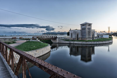 Bridge over river by buildings against sky