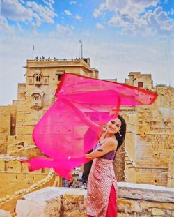 Woman holding pink umbrella against building