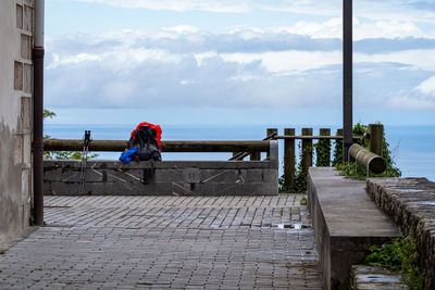 Woman sitting on bench by sea against sky