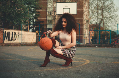 Beautiful young woman playing with basketball on court