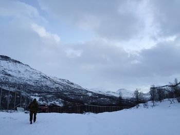 Rear view of man walking on snow field by mountains against sky