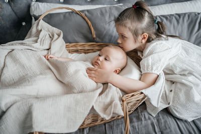 Girl taking care of her younger sister on the bed wicker basket hugs