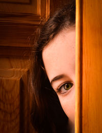 Close-up portrait of girl peeking through wooden door