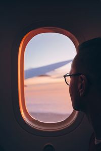 Close-up of man looking through airplane window