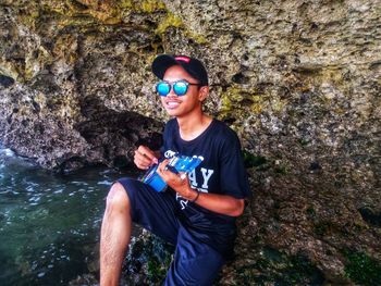 Young woman wearing sunglasses holding rock in water