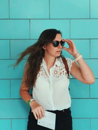 Woman wearing sunglasses while standing against wall