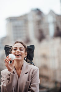 Portrait of young woman holding camera while standing outdoors