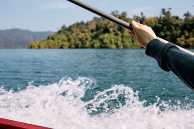 Midsection of man holding oar at sea against sky