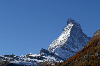 Low angle view of snowcapped mountains against clear blue sky