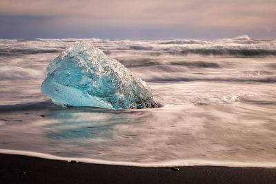 Sea waves splashing on beach against sky during sunset