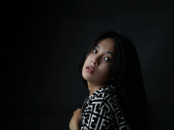 Portrait of woman looking away against black background