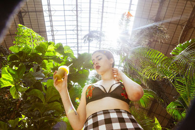 Low angle view of young woman with short hair holding juice against plants